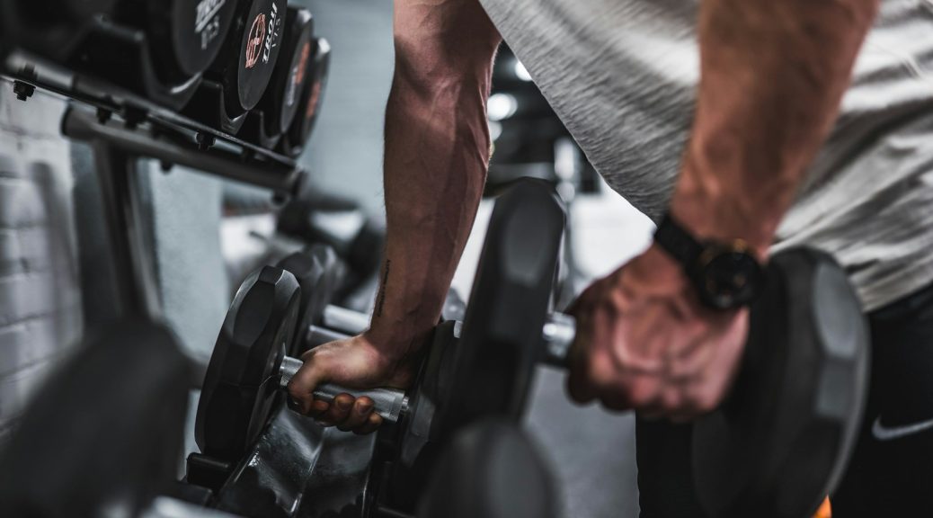 person in gray shirt holding black dumbbell