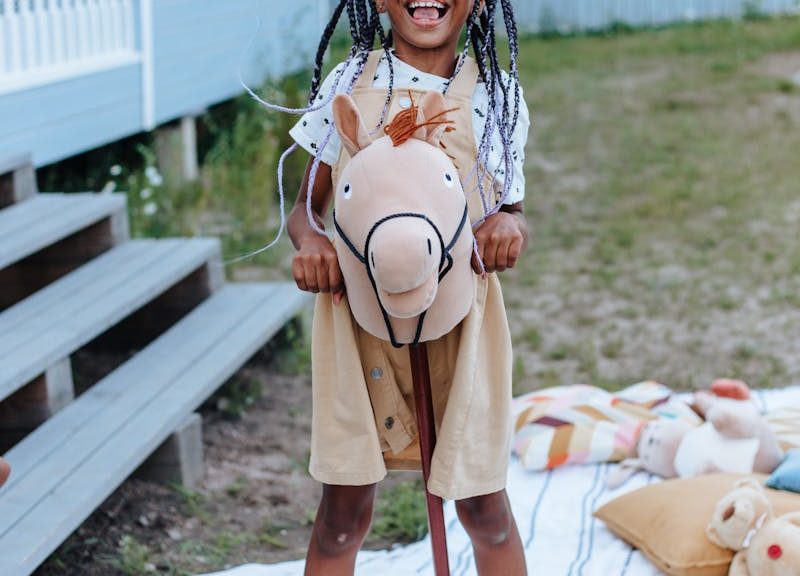 A happy girl enjoys a sunny day playing with a toy horse in the backyard.